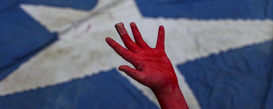 Une performance montre une main couverte de peinture rouge, symbolisant le sang, devant un drapeau chilien pour rendre hommage aux manifestants tués lors des manifestations de 2019 au Chili. [KEYSTONE - Esteban Felix / AP Photo]