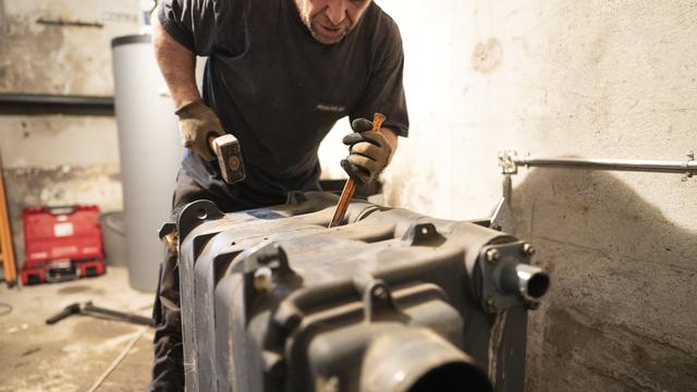 Un chauffagiste démonte une chaudière fioul dans le sous-sol d'une maison. Elle sera remplacée par une pompe à chaleur avec sonde géothermique. [Keystone - Gaetan Bally]