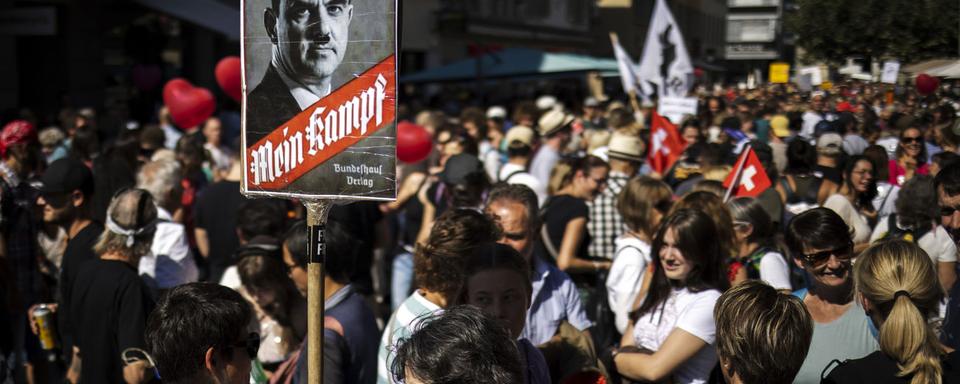 Lors d'une manifestation anti-mesures sanitaires, une manifestante brandit une pancarte avec un photomontage du conseiller fédéral Alain Berset en Adolf Hitler, le 18 septembre 2021 à Winterthour. On peut y lire "Mein Kampf" (Mon combat), titre du fameux livre de Hitler, et "Impfen macht frei" (La vaccination rend libre), une allusion à "Arbeit macht frei", slogan affiché à l'entrée de plusieurs camps de concentration nazis durant la Deuxième Guerre mondiale. [KEYSTONE - Michael Buholzer]