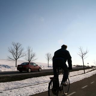 Un individu à vélo roule sur une route enneigée en hiver. [Depositphotos - jeancliclac]