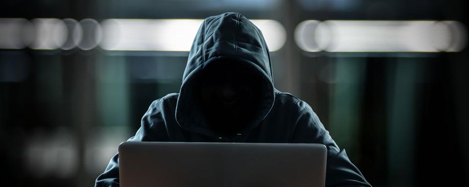 Un hacker se tient derrière son écran d'ordinateur. [Depositphotos - minervastock]