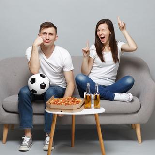 Un femme s'enthousiasme à propos d'un match de foot alors qu'un homme est déprimé. [Depositphotos - dmvasilenko]