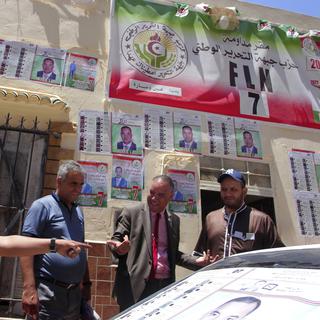 Des hommes discutent devant des affiches électorales à Ouessara, en Alégie le 12 juin 2021. [Keystone - AP Photo/Fateh Guidoum]