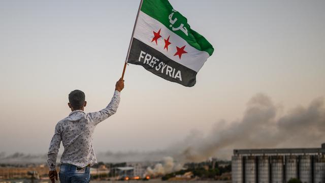 Un Syrien brandit un drapeau de l'opposition au régime alors que la fumée s'échappe de l'offensive turque contre la ville de Tal Abyad. [AFP - BULENT KILIC]