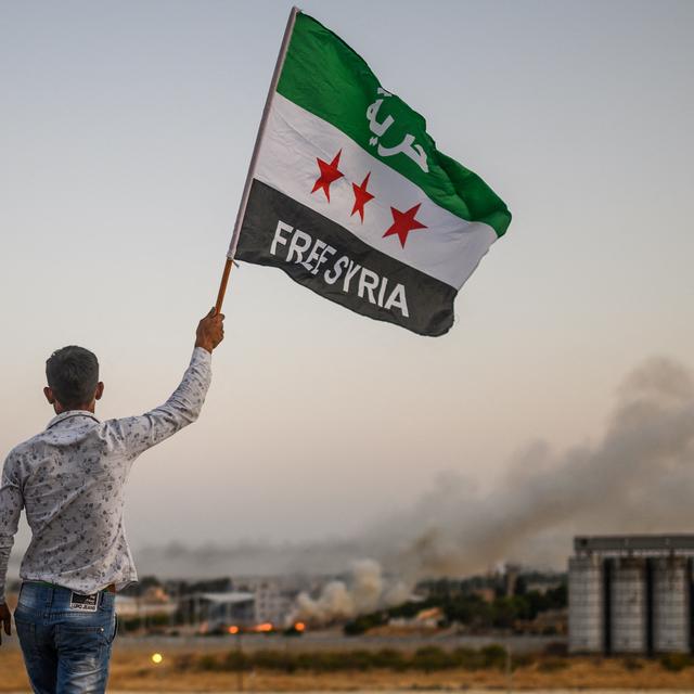 Un Syrien brandit un drapeau de l'opposition au régime alors que la fumée s'échappe de l'offensive turque contre la ville de Tal Abyad. [AFP - BULENT KILIC]