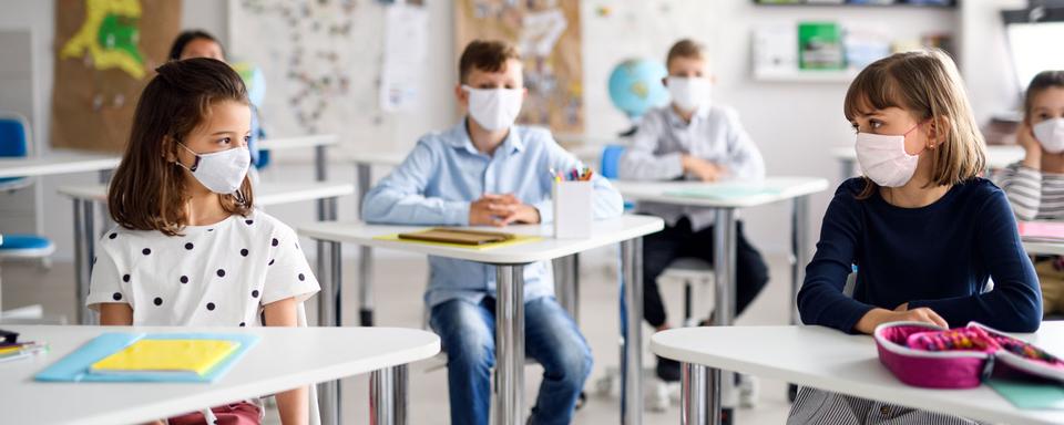 Des enfants qui portent un masque chirurgical sont assis dans une classe. [Depositphotos - halfpoint]