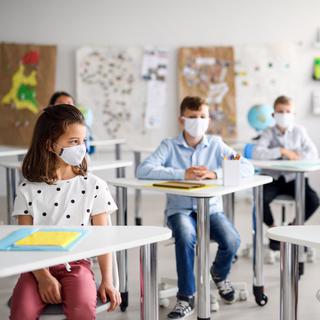 Des enfants qui portent un masque chirurgical sont assis dans une classe. [Depositphotos - halfpoint]