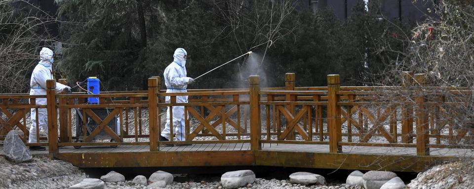 Des agents en habits de protection répandent du spray désinfectant sur le mobilier urbain, le 13 janvier 2021 dans une ville de la province du Hebei en Chine. [AP/Keystone - Wang Xiao]