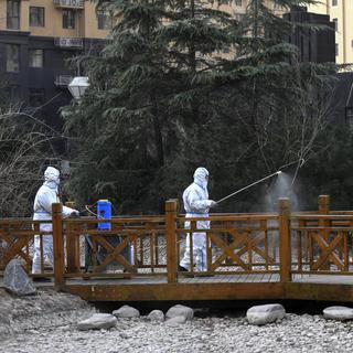 Des agents en habits de protection répandent du spray désinfectant sur le mobilier urbain, le 13 janvier 2021 dans une ville de la province du Hebei en Chine. [AP/Keystone - Wang Xiao]