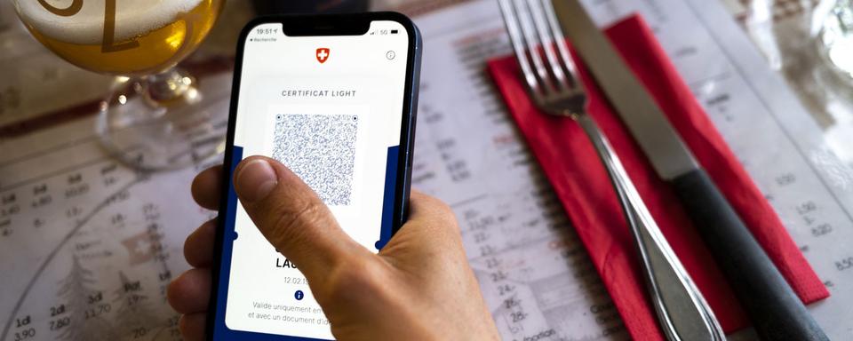 Une personne tient dans sa main un smartphone affichant un certificat Covid dans un restaurant. [Keystone - Laurent Gillieron]