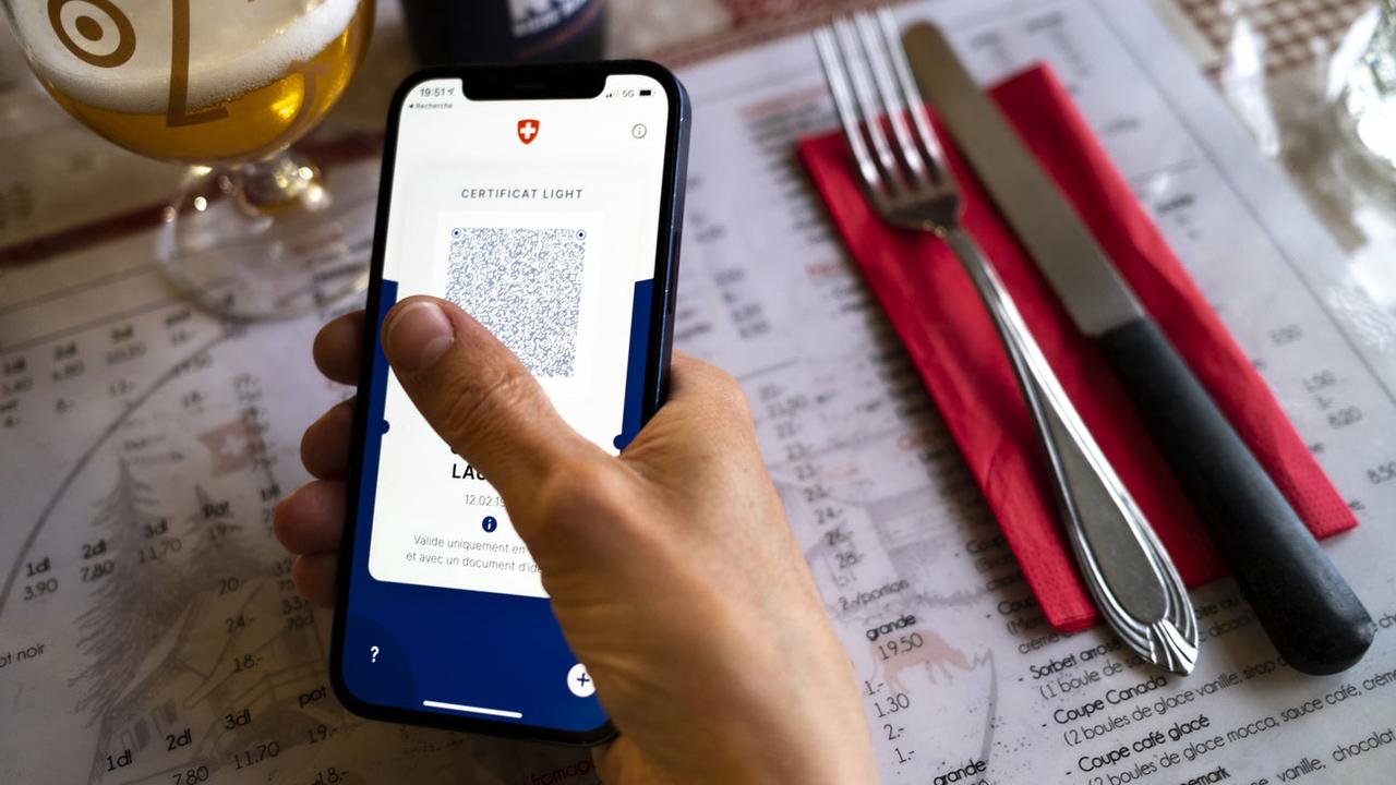 Une personne tient dans sa main un smartphone affichant un certificat Covid dans un restaurant. [Keystone - Laurent Gillieron]