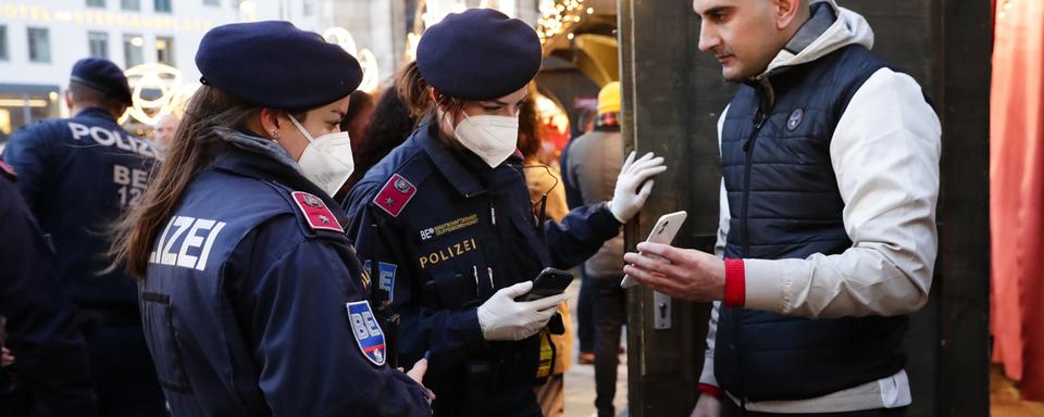 Deux policières vérifient le statut vaccinal d'un individu sur son smartphone. [AP Photo/Keystone - Lisa Leutner]