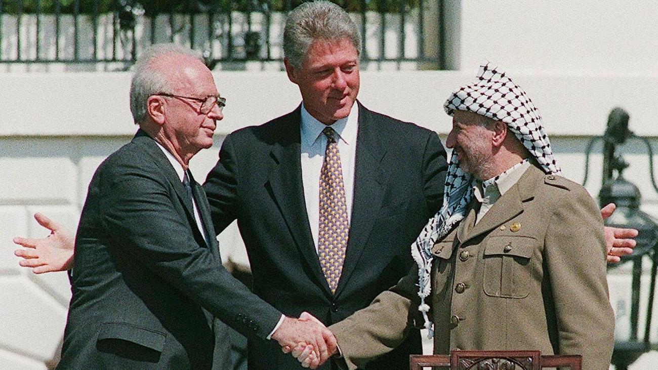 Le Président palestinien Yasser Arafat (à droite) lors de sa poignée de main historique avec le Premier Ministre israélien Yitzhak Rabin (à gauche) sur la pelouse de la Maison Blanche alors que les deux leaders sont réunis par le Président américain Bill Clinton dans le cadre des accords d'Oslo, le 13 septembre 1993. Ces accords devaient poser les premiers jalons d'une résolution du conflit israélo-palestinien. [KEYSTONE/EPA/ISRAELI GOVERNMENT - AVI OHAYON]