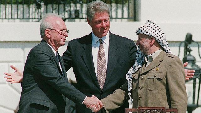 Le Président palestinien Yasser Arafat (à droite) lors de sa poignée de main historique avec le Premier Ministre israélien Yitzhak Rabin (à gauche) sur la pelouse de la Maison Blanche alors que les deux leaders sont réunis par le Président américain Bill Clinton dans le cadre des accords d'Oslo, le 13 septembre 1993. Ces accords devaient poser les premiers jalons d'une résolution du conflit israélo-palestinien. [KEYSTONE/EPA/ISRAELI GOVERNMENT - AVI OHAYON]