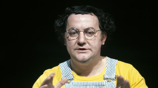 Coluche avec sa légendaire salopette bleue à rayures. [Ina via AFP - Jacques Chevry]