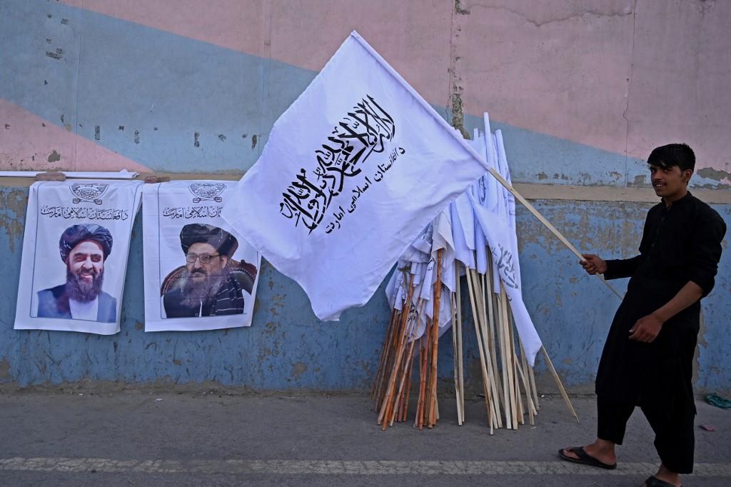 Un vendeur de rue brandit un drapeau taliban à côté de posters représentant deux dirigeants talibans: Amir Khan Muttaqi (gauche) et le mollah Abdul Ghani Baradar (droite). Kaboul, le 27 août 2021. [AFP - Aamir Qureshi]