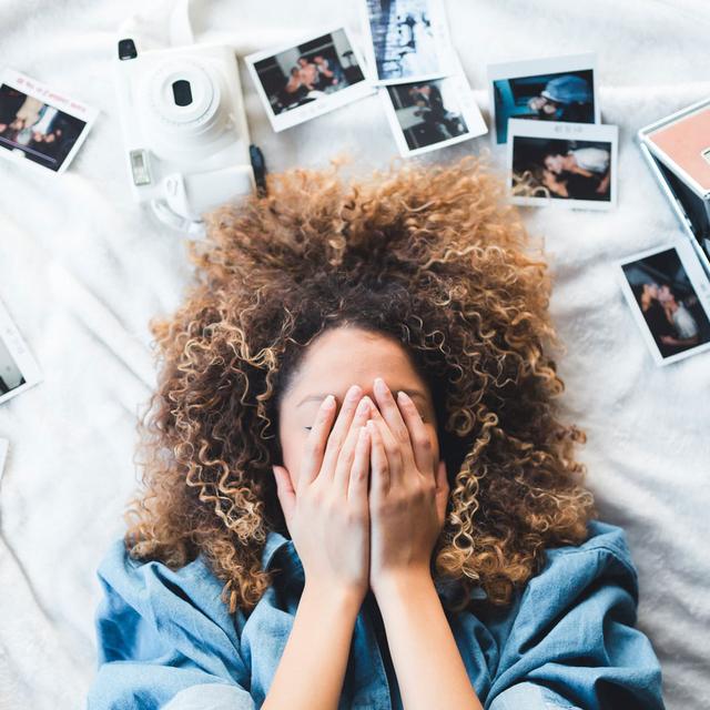 Une femme se tient la tête dans les mains devant des photos. [Depositphotos - ian dooley]