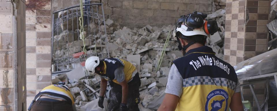 Des Casques blancs à la recherche de victimes sous les décombres d'un bâtiment détruit. [AP/Keystone - Syrian Civil Defense White Helmets]