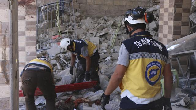 Des Casques blancs à la recherche de victimes sous les décombres d'un bâtiment détruit. [AP/Keystone - Syrian Civil Defense White Helmets]