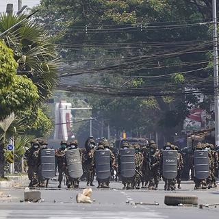 Des soldats birman avancent derrière des boucliers en direction de la foule dans une rue de Rangoun, capitale de la Birmanie, le 2 mars 2021. [AP/Keystone]