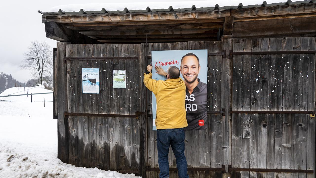 Un militant accroche une affiche de campagne pour le socialiste Mathias Reynard, en course pour un siège au Conseil d'Etat valaisan. [Keystone - Jean-Christophe Bott]