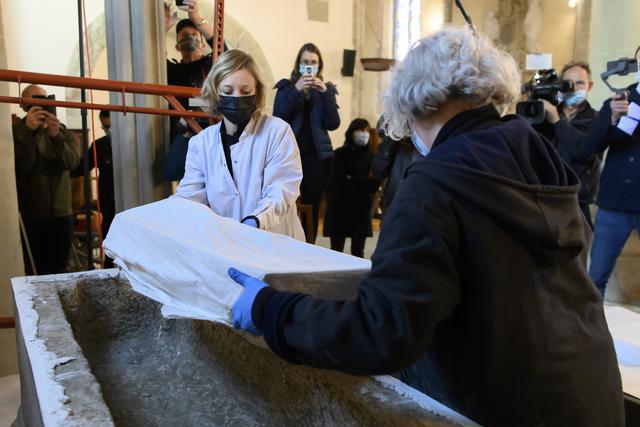 Laure-Anne Kupfer, conservatrice-restauratrice d'objets archéologiques et ethnographiques au Musée cantonal d'archéologie et d'histoire de Lausanne (gauche) et Lucie Steiner, archéologue spécialiste en archéologie funéraire (droite) soulèvent d'un sarcophage une boîte recouverte d'un tissu, lors de l'ouverture du tombeau de la Reine Berthe. Payerne, le 20 mai 2021. [KEYSTONE - Anthony Anex]