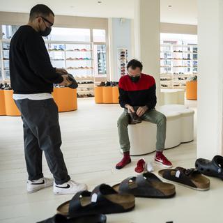 Un vendeur et un acheteur choisissent une paire de chaussure dans le magasin de chaussures "Pompes Funèbres" lors de la réouverture des magasins pendant la crise du Coronavirus (Covid-19). [KEYSTONE - JEAN-CHRISTOPHE BOTT]