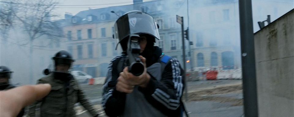 Policier pointant son lanceur de balles de défense (ou "Flash-Ball") à bout portant durant une manifestation de gilets jaunes. [Jour2fête/Le Bureau]