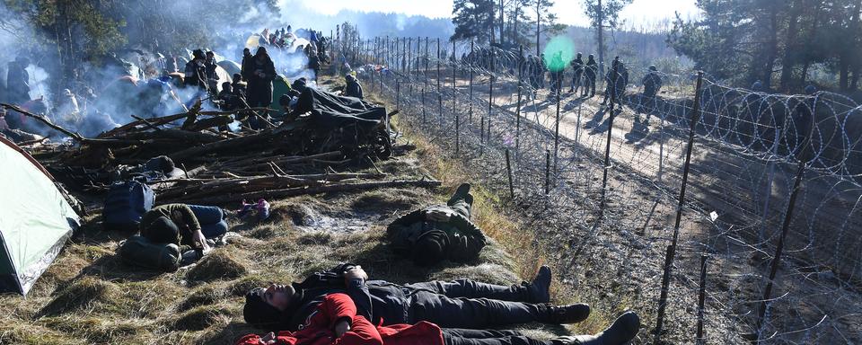 Des réfugiés gisent sur le sol dans un camp de migrants à la frontière entre la Pologne et la Biélorussie. [AFP - Viktor Tolochko / Sputnik]