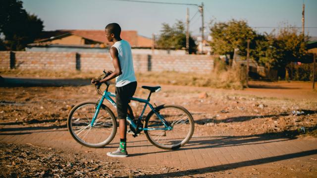 Une jeune homme africain pousse un vélo. [Unsplash - Rachel Martin]