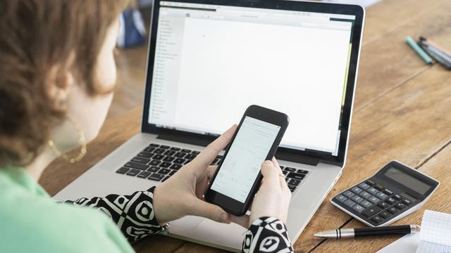 Une femme utilisant son smartphone et travaillant sur son ordinateur. [AFP - Frédéric Cirou / AltoPress]