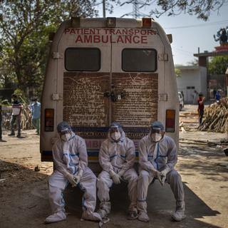 Des travailleurs épuisés se reposent derrière l'ambulance qui vient d'amener des corps destinés à la crémation. New Delhi, le 24 avril 2021. [Keystone/AP photo - Altaf Qadri]