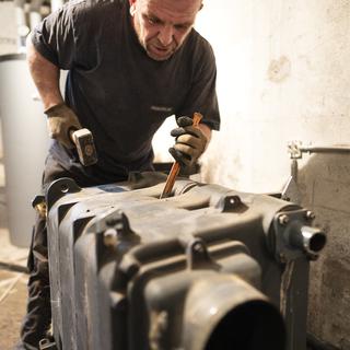 Un chauffagiste démonte une chaudière fioul dans le sous-sol d'une maison. Elle sera remplacée par une pompe à chaleur avec sonde géothermique. [Keystone - Gaetan Bally]