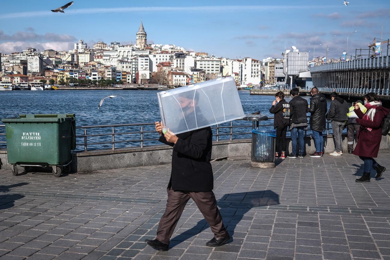 Un homme portant un masque transporte une caisse en plastique. Istanbul, le 21 février 2021. [Keystone/epa - Sedat Suna]