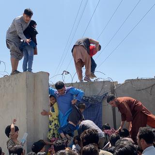 Des habitants de Kaboul tentent d'escalader le mur d'enceinte de l'aéroport international dans l'espoir de fuir les Talibans. [EPA/Keystone]