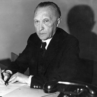 Image d'archive en noir et blanc du portrait de Konrad Adenauer à son bureau, tenant un stylo-plume à la main. [KEYSTONE/AP Photo/Str]