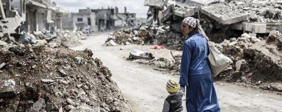 Une femme kurde de Syrie avec son enfant dans les ruines de la ville de Kobane, en mars 2015. [AFP - YASIN AKGUL]