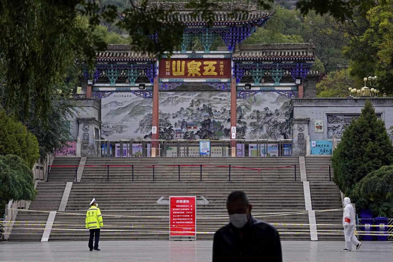 Un policier et un travailleur en tenue de protection montent la garde à l'entrée de la montagne Wuquan qui a été fermée pour empêcher les visiteurs de se rassembler dans la ville de Lanzhou, dans la province chinoise du Gansu. [KEYSTONE - Chinatopix / AP]