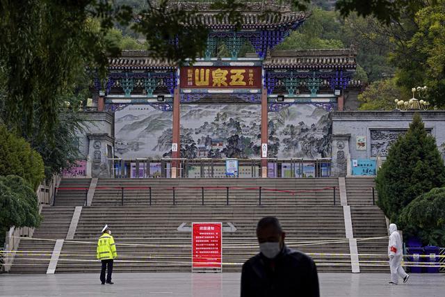 Un policier et un travailleur en tenue de protection montent la garde à l'entrée de la montagne Wuquan qui a été fermée pour empêcher les visiteurs de se rassembler dans la ville de Lanzhou, dans la province chinoise du Gansu. [KEYSTONE - Chinatopix / AP]