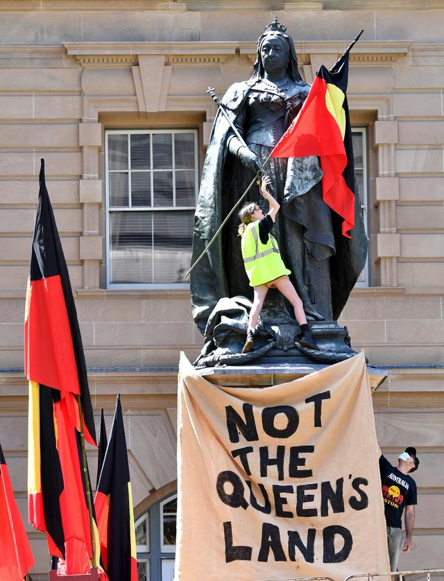 Un drapeau aborigène et le slogan "Ce n'est pas la terre de la reine" sont accroché sur une statue de la Reine Victoria, à Brisbane, le 26 janvier 2021. [Keystone/epa - Darren England]