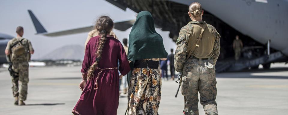 Une soldate américaine marche avec une famille afghane sur le tarmac de l'aéroport de Kaboul, le 24 août 2021. [Keystone/AP - Sgt. Samuel Ruiz/U.S. Marine Corps]