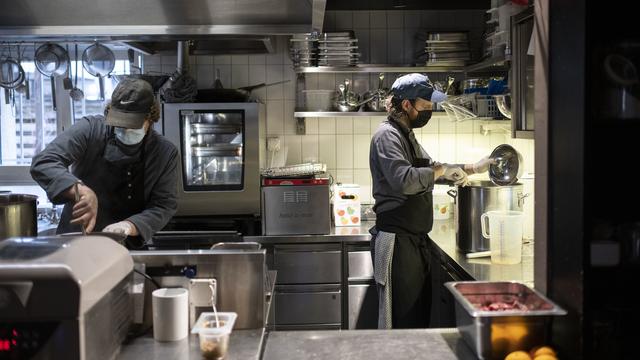 Dans la cuisine d'un restaurant zurichois, un chef et un cuisinier masqués s'affairent à la préparation des plats. [Keystone - Christian Beutler]