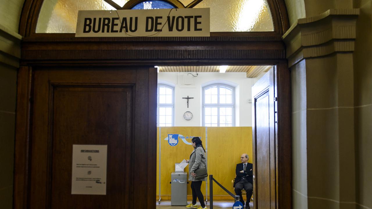 Une personne glisse un bulletin de vote dans l'urne lors d'une votation à Fribourg. [KEYSTONE - JEAN-CHRISTOPHE BOTT]