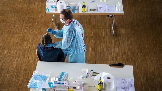 Des personnes font un test rapide dans un centre de dépistage du Covid. [Keystone - Jean-Christophe Bott]