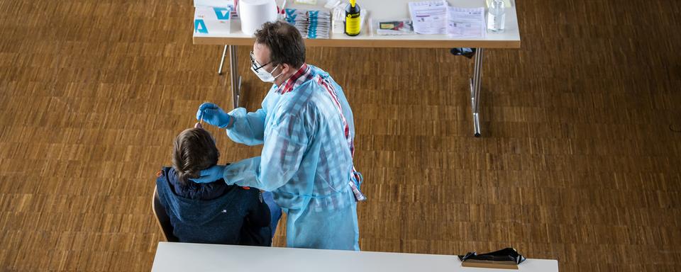 Des personnes font un test rapide dans un centre de dépistage du Covid. [Keystone - Jean-Christophe Bott]