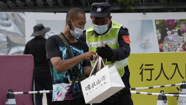 Un livreur contrôlé par un agent de sécurité dans une rue de Pékin. [AP/Keystone - Ng Han Guan]