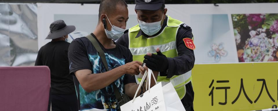 Un livreur contrôlé par un agent de sécurité dans une rue de Pékin. [AP/Keystone - Ng Han Guan]