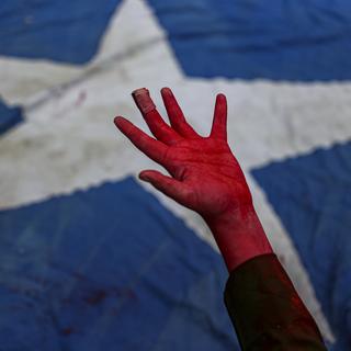 Une performance montre une main couverte de peinture rouge, symbolisant le sang, devant un drapeau chilien pour rendre hommage aux manifestants tués lors des manifestations de 2019 au Chili. [KEYSTONE - Esteban Felix / AP Photo]