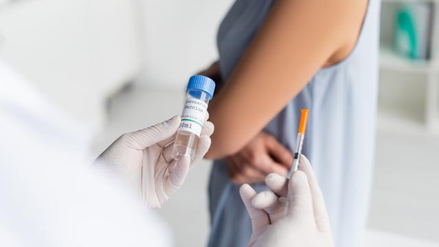 Médecin tenant le vaccin contre le covid et une seringue s'apprêtant à piquer une patiente. [Depositphotos - IgorVetushko]