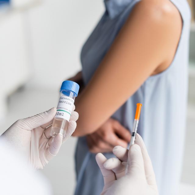 Médecin tenant le vaccin contre le covid et une seringue s'apprêtant à piquer une patiente. [Depositphotos - IgorVetushko]